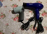 Braun Cosmo 1000 and Conair hair dryers side by side on floral fabric with coiled power cords