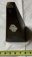 Side view of the antique wooden metronome placed beside a measuring tape indicating approximately 9 inches in height.