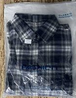 Photo of new XL plaid shirt in original plastic packaging showing folded collar, button-up front, and packaging text.