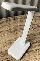 White desk lamp standing upright on a marble surface, showing front angle with light head angled slightly forward.