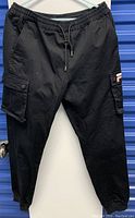 Front view of black FILA cargo pants hanging on hanger, showing elastic waistband and side pockets.