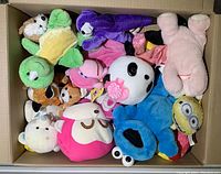 Box full of assorted colorful plush toys including a green turtle, pink flamingo, panda, Minion, and Cookie Monster among others.