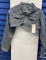 Front view of the new with tags blue denim cropped jean jacket hanging on a hanger