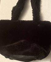 Front view of black faux fur tote bag showing plush texture, thick handles, and leather-like base.