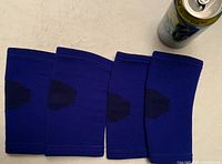 Top view of four blue elastic knee/elbow pads laid out with a can for size reference.