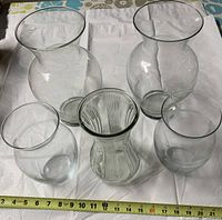 Top-down view of all five glass vases showing their shapes and relative sizes with measuring tape for scale.