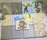Full view showing all 13 canvas art pieces arranged on floor, featuring flowers, monkeys, birds, and duck images.