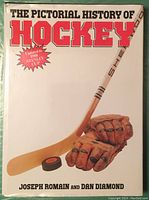 Front cover of The Pictorial History of Hockey book showing title, authors, hockey stick, gloves, and puck.