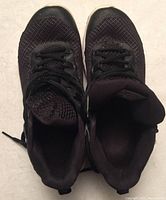 Top-down view of pair of black Under Armour boys shoes, showing mesh fabric, laces, and padded tongue.