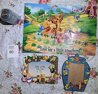 Photo showing Winnie the Pooh picnic placemat and two picture frames on floral tablecloth with soda can for scale.