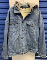 Front view of the denim jacket showing button closure, chest pockets, and attached grey hood.