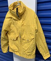 Front view of yellow jacket hanging on hanger, showing zipper, pockets, and collar.