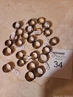 Photo showing 27 assorted metal rings laid out on a flat surface, each with a small size tag attached.