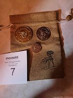 Overview of the three coins and tan drawstring pouch with embroidered flower logo on a white surface