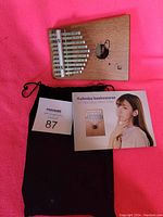 Wooden kalimba on pink cloth with black drawstring bag and music book beside it.