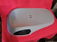 White Ozeri digital baby scale with contoured tray and display panel shown against a red background.