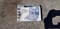 Gray hard plastic case labeled '62 pieces Drill/Driver Accessory Set' shown closed outdoors on pavement.
