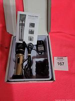 Photo shows a cordless rechargeable professional hair clipper in metallic silver and black colors, power charger, several clipper guide comb attachments, instruction manual, and white plastic tray inside a box against a red background.