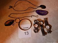 Photo showing three watches, two necklaces with agate pendants, one bracelet, and one keychain arranged on a beige surface.