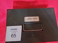 Top view of closed black metal cash box with handle and a label 'CASH BOX'.