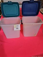 Front view of two rectangular storage pails with green and blue hinged lids on a red surface.