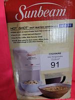 Photo of Sunbeam Hot Shot hot water dispenser box showing brand, model 3011-33 and product features including 475ml capacity, easy heat and dispense for tea, coffee, baby formula, cereal.