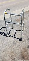 Front view of aluminum walker with two small front wheels and rubber hand grips, showing adjustable height mechanism.