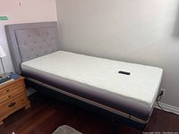 Full view of the adjustable twin bed with mattress and tufted gray headboard, including remote on mattress.