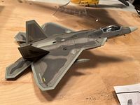 Side and top view of die cast F-22 Raptor model showing gray camouflage paint and detailed surface panel lines.