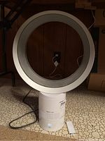 Dyson Cool bladeless fan in white with power cord and remote control on floor.