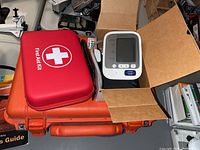 Orange Pelican 1500 EMS Kit case with red First Aid Kit and Omron blood pressure monitor on top, displayed in open and closed views.