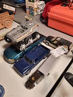 Five model vehicles on a table including a UPS semi-truck and trailer, two pickup trucks, a convertible car, and a gray Bigtrak X toy vehicle.