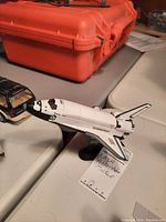 Image of the NASA Atlantis space shuttle model on a table with orange case in background, showing the model's left side and nose detail.