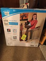 Box front showing the product image, woman holding a basket with the metal gate installed in a stairway.