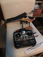 Hummingbird RC helicopter positioned next to the Elite 6 remote control and instruction manual on a chair, shown to provide overall view of the lot contents.