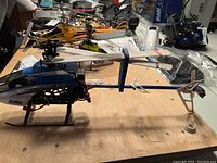 Eflite Blade SR RC helicopter on a wooden surface alongside other RC helicopters and parts.