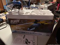 Blue and white Eflite Blade SR electric remote control helicopter on Styrofoam insert inside original box with instructions visible.