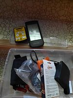Overview of all included items inside the plastic bin, showing the battery tester, Rotel device, tool, handwarmers, Garmin screen, and packaging.