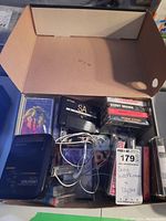 Open cardboard box containing Sony Walkman WM-FX305, multiple cassette tapes in plastic cases, and white wired headphones.