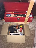 Red metal toolbox open showing contents of hand tools such as scissors, putty spreader, precision wrench, screwdriver, masking tape, black glove, and 3M branded sanding discs box.