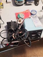 Weller soldering iron and stand, power unit, and two small containers labeled Kester soldering and acid paste flux on table.