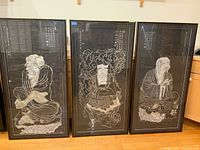 Photo showing the full set of three framed Asian rubbings with black mat and frames on wooden floor