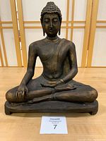 Front view of large resin Buddha figure seated with serene expression, lotus pose, on sculpted base with felt bottom.