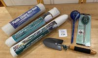 Overview of garden lot items including plastic chicken wire mesh, frost protection fleece rolls, hand trowel, and water moisture meter in packaging
