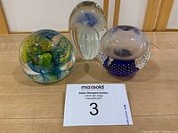 Three glass paperweights displayed together showing varied shapes and internal designs.