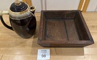 Photo showing ceramic tea pot and wooden square tray side by side on a table.