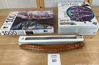 Lot contents showing Moraine Lake 1000-piece puzzle, Harry Potter 3D puzzle box unopened, and wooden snake puzzle in box.