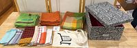 Two green pillow covers, assorted place mats, cloth bag with shopping cart logo, and decorative storage box
