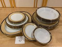Stacked display of assorted Noritake china pieces with gold and black rim including plates and bowls arranged for clear view of pattern and sizes