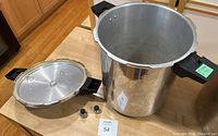 Metal pressure cooker with one lid placed beside it along with two safety valves shown on the countertop.